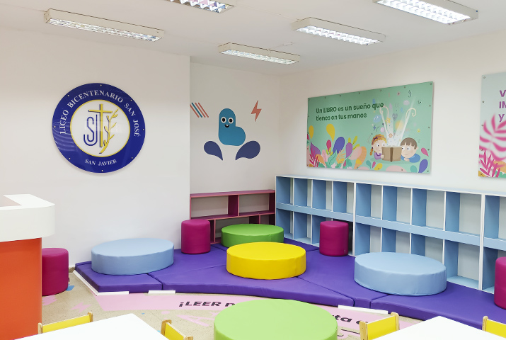 Detalle de una biblioteca que muestra parte del mobiliario de la sala, tales como repisas, mesas, gráficas murales que estimulan la lectura y el aprendizaje, pufs de esfuma y piso con diseños adhesivos. Se aprecia el logo del Liceo sobre acrílico.
