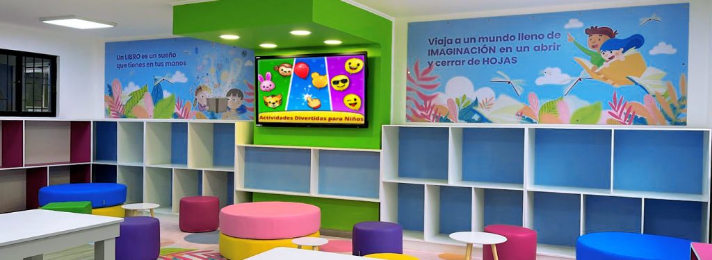 Detalle de una gran y colorida biblioteca que muestra parte del mobiliario de la sala, tales como repisas, mesas, gráficas murales que estimulan la lectura y el aprendizaje, pufs de esfuma y piso con diseños adhesivos.